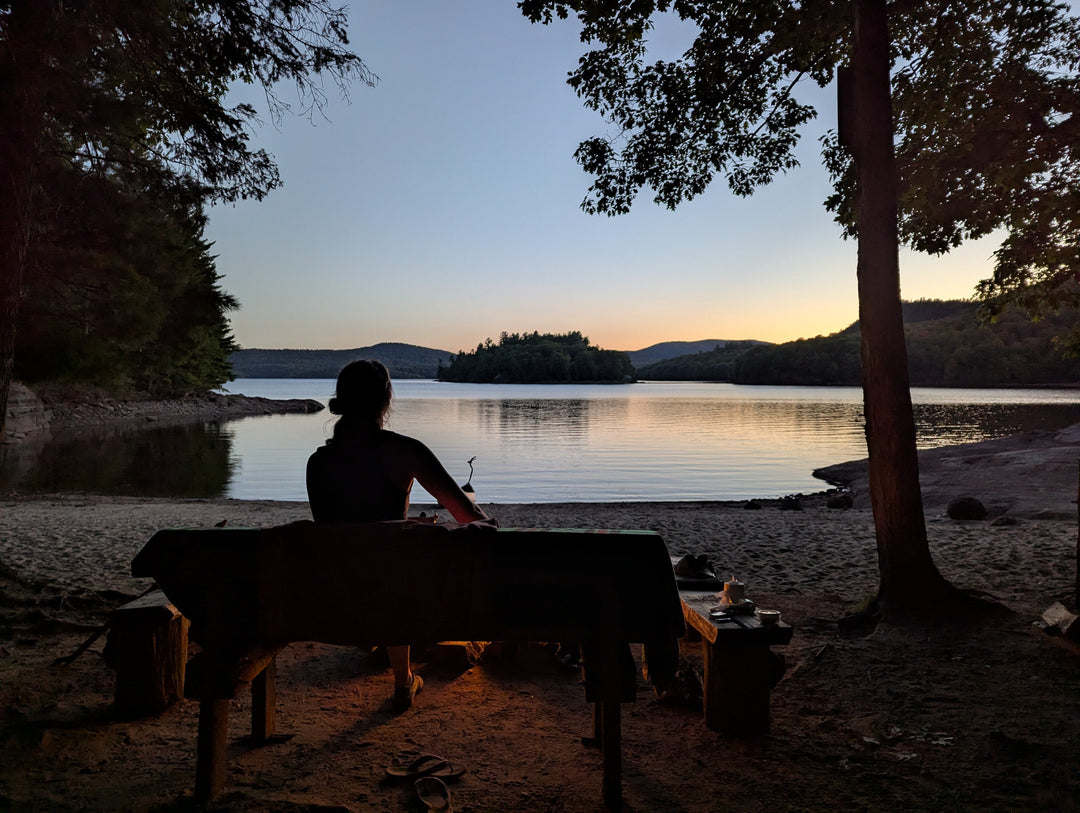 Beautiful sunset over serene lake and beach with woman by campfire - Bromont Media