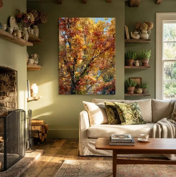 A large vertical canvas print of an autumn tree with vibrant orange, yellow, and red leaves, displayed on a sage green wall in a cozy, sunlit living room with a sofa, fireplace, and wooden coffee table.