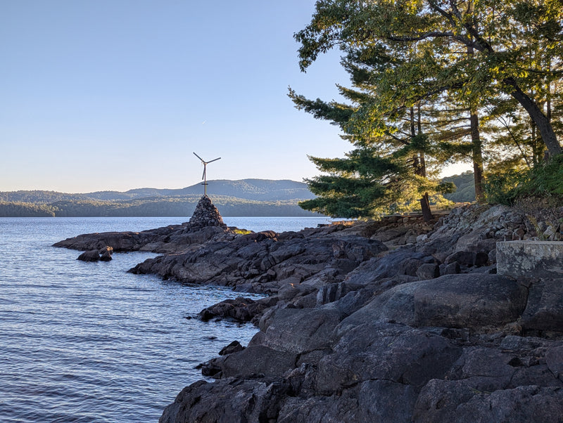 A small windmill generator turbine on a rocky island serene landscape - Bromont Media