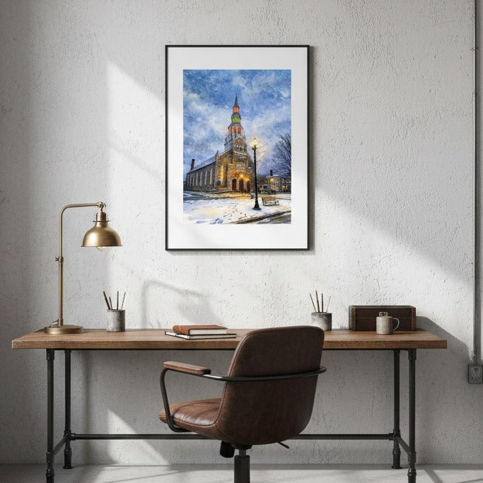 Home office with wooden desk, leather chair, and framed artwork of a snowy street with a church.