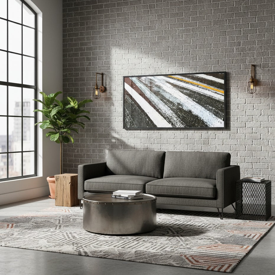 Modern living room with a gray sectional sofa, round metal coffee table, and abstract painting on a brick wall by Studio Shefford