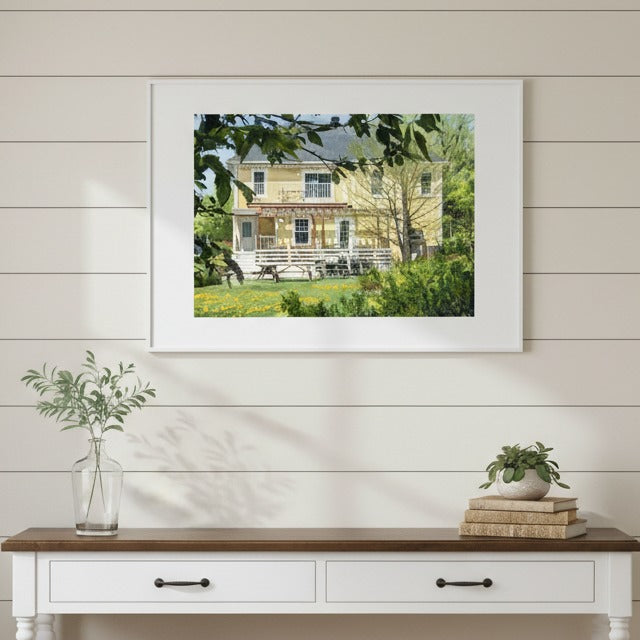 Framed artwork of a yellow house on a wall above a wooden console table - Studio Shefford